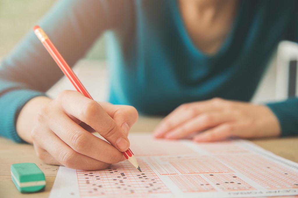 A student writing on paper with a pencil. 