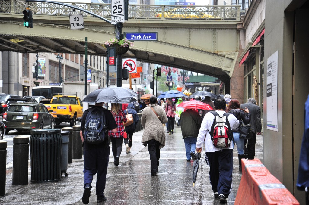 People walk with umbrellas in the rain towards Grand Central Station on Park Avenue in New York City.