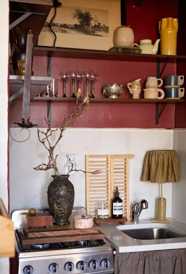 Cozy kitchen corner with a vintage stove, decorative vases, glassware, and a wooden cutting board.