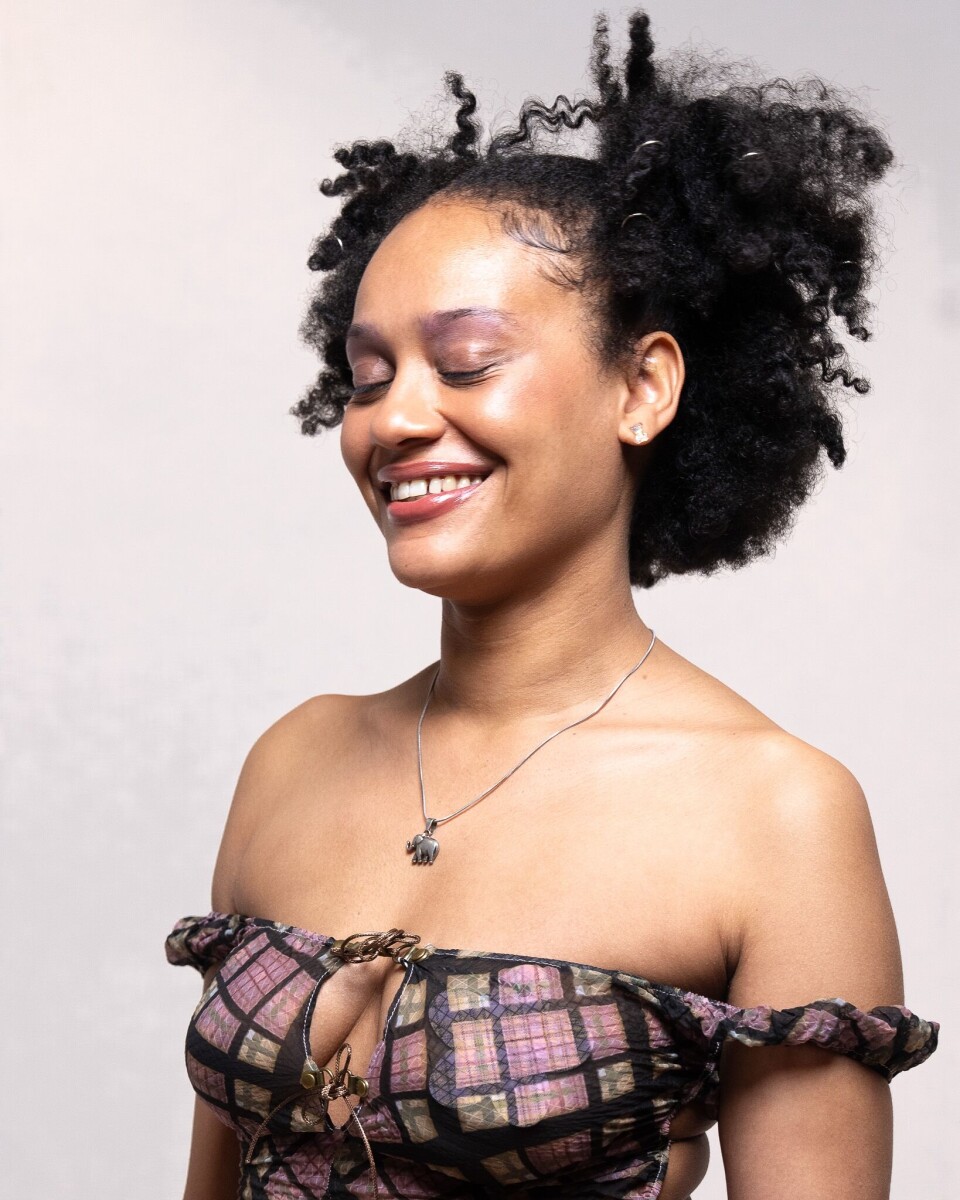 Smiling woman with curly hair posing in a studio against a light backdrop