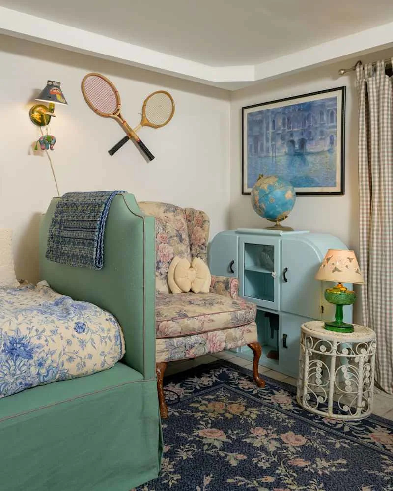 Cozy bedroom corner with a green bed, floral armchair, blue globe, and vintage tennis rackets on the wall.