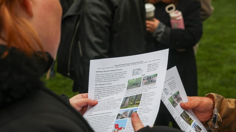 Attendees at the Kings Point Park rally look over a fact...