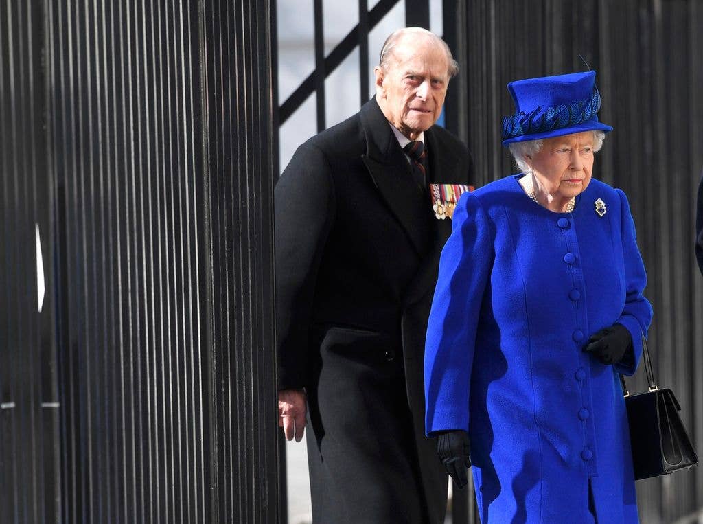 Prince Philip in a black coat walking with the Queen in a blue outfit