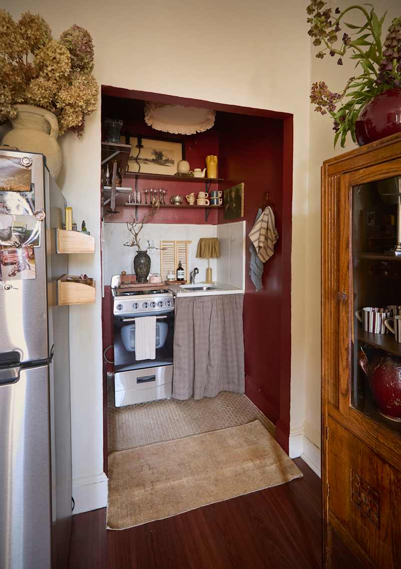 Cozy kitchen nook with a gas stove, sink, and wooden shelves displaying glassware and decor, accented by a red wall.