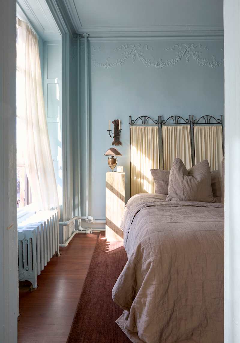 Cozy bedroom with a light blue wall, a bed with beige bedding, a wooden nightstand, and a vintage lamp.