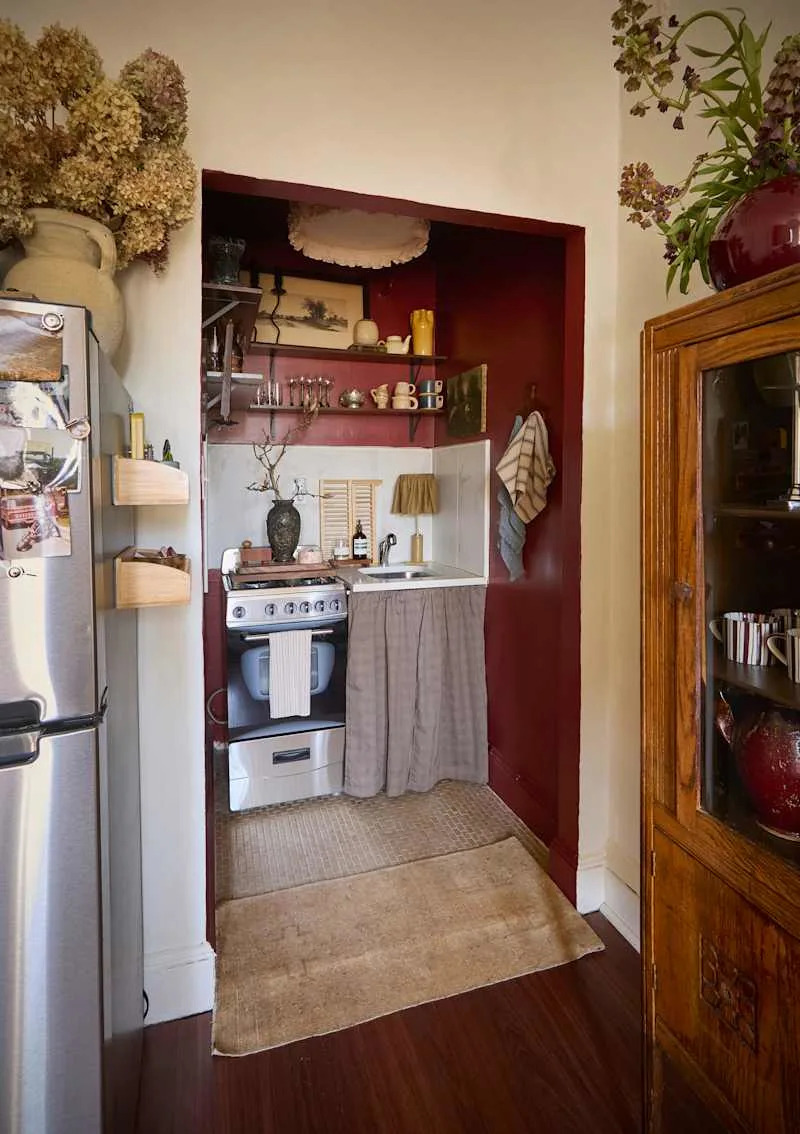 Cozy kitchen nook with a gas stove, sink, and wooden shelves displaying glassware and decor, accented by a red wall.