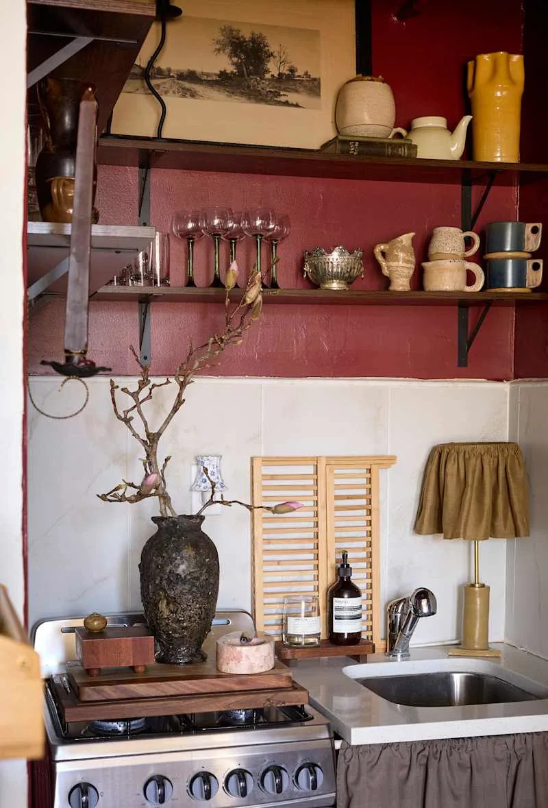 Cozy kitchen corner with a vintage stove, decorative vases, glassware, and a wooden cutting board.