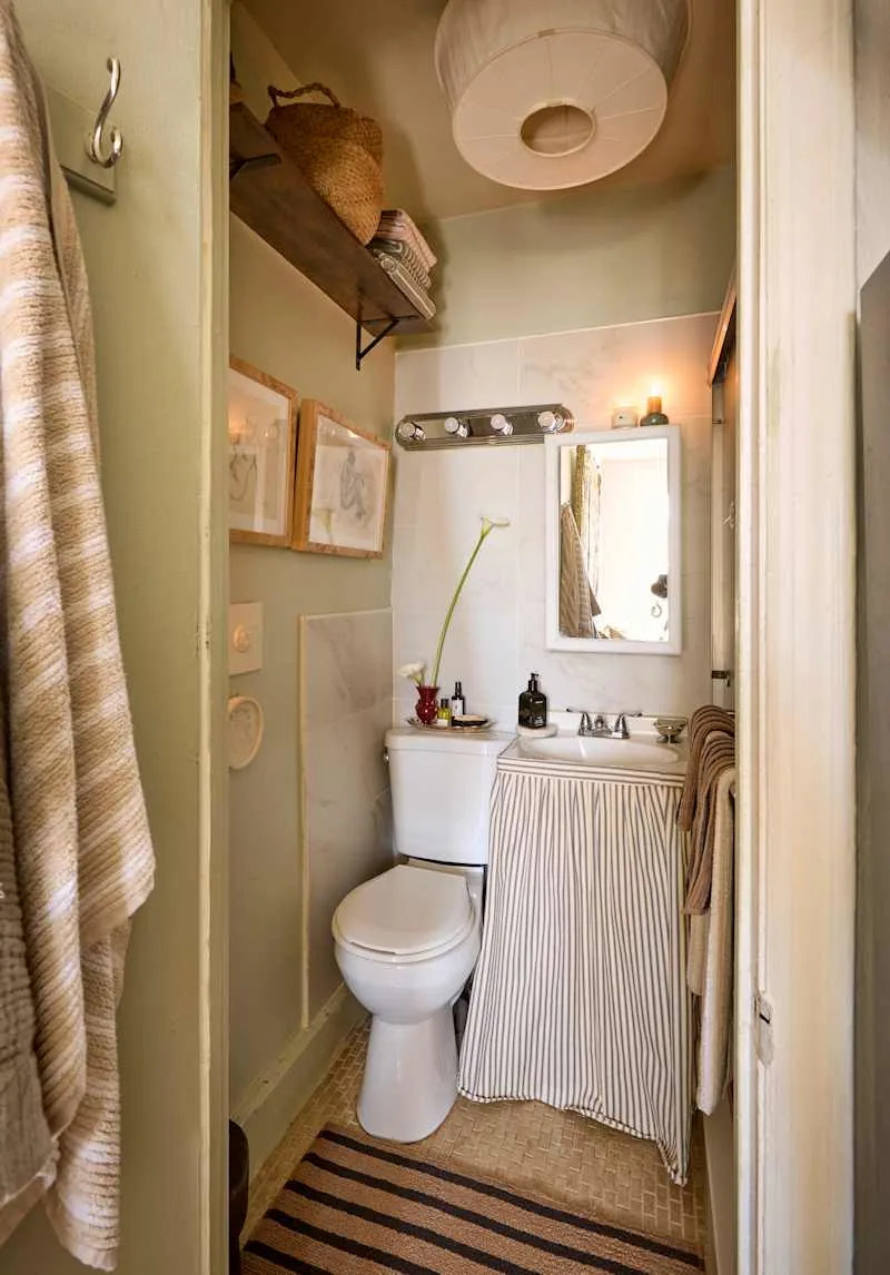 Small bathroom with a striped shower curtain, a white toilet, and a sink with a mirror, featuring green walls and decorative items.