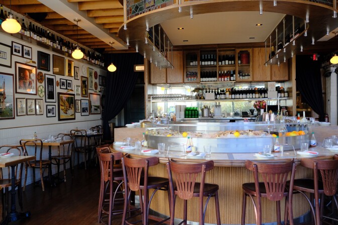 A restaurant interior, including multiple chair toward a bar. The bar also includes a container with ice and lemons.