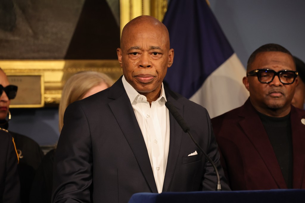 Mayor Eric Adams speaking at a podium with others behind him.