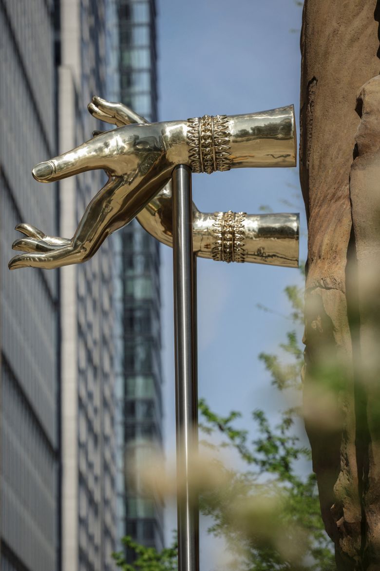 Steel hands, supported by tall rods, appear to float slightly away from the sculpture's sandstone limbs.
