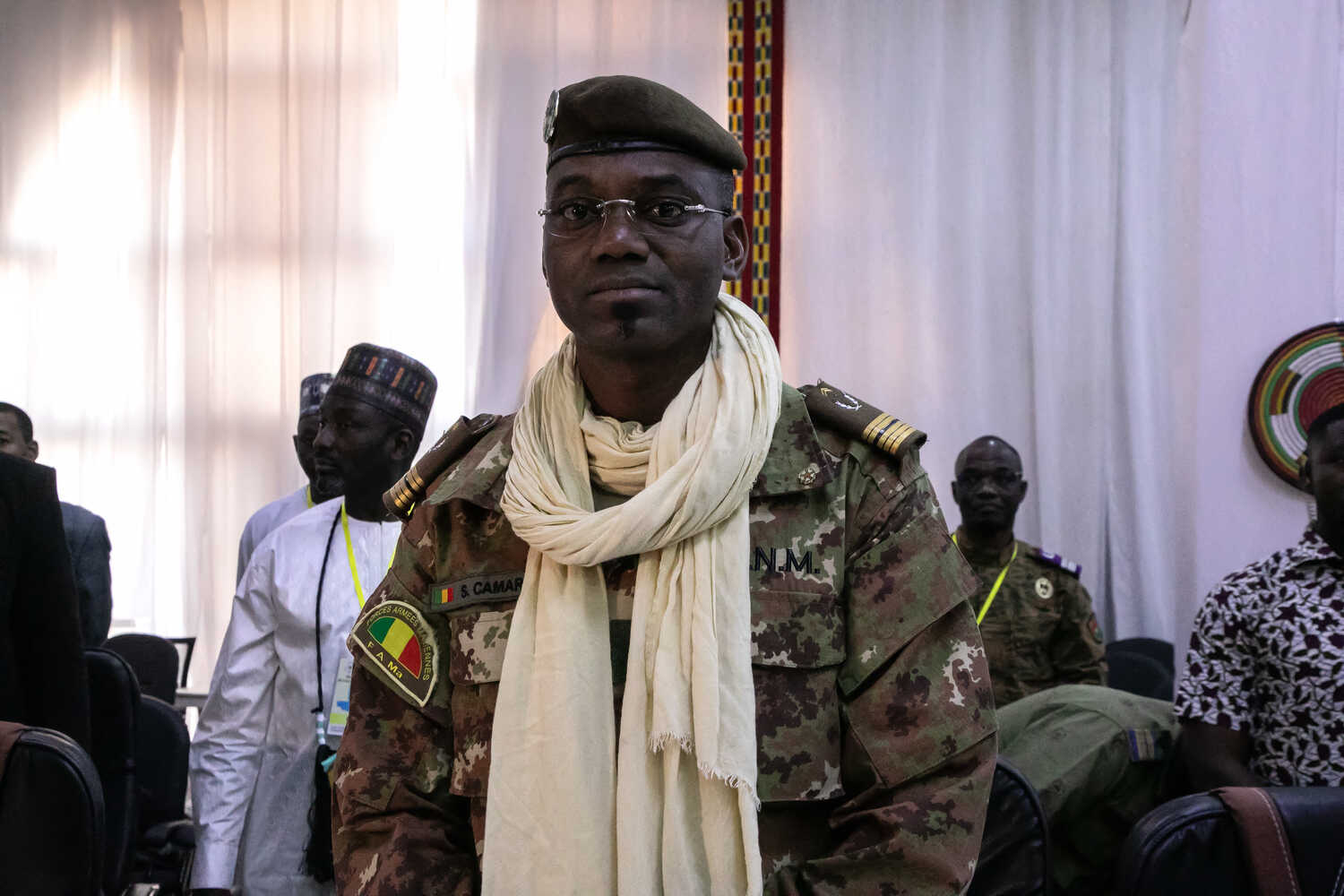 A man in a camouflage uniform and military beret, with a white scarf.