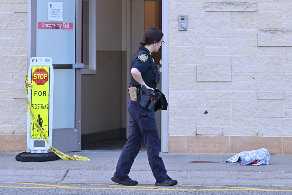 A police officer walks past a closed Target store entrance with crime scene tape and a bloodied towel on the ground.
