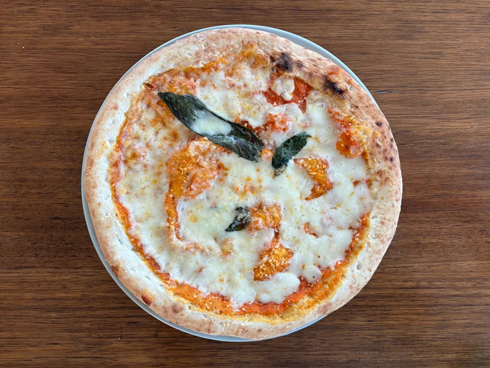 Pizza with melted cheese, tomato sauce, and basil leaves on a wooden table