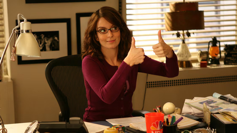 Liz Lemon giving two thumbs up from behind her desk in 30 Rock