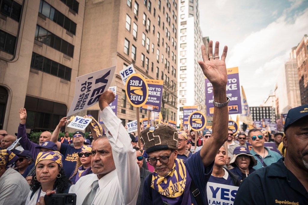 People rally in the street, holding signs that read "YES I AM READY TO STRIKE" and "32BJ SEIU."