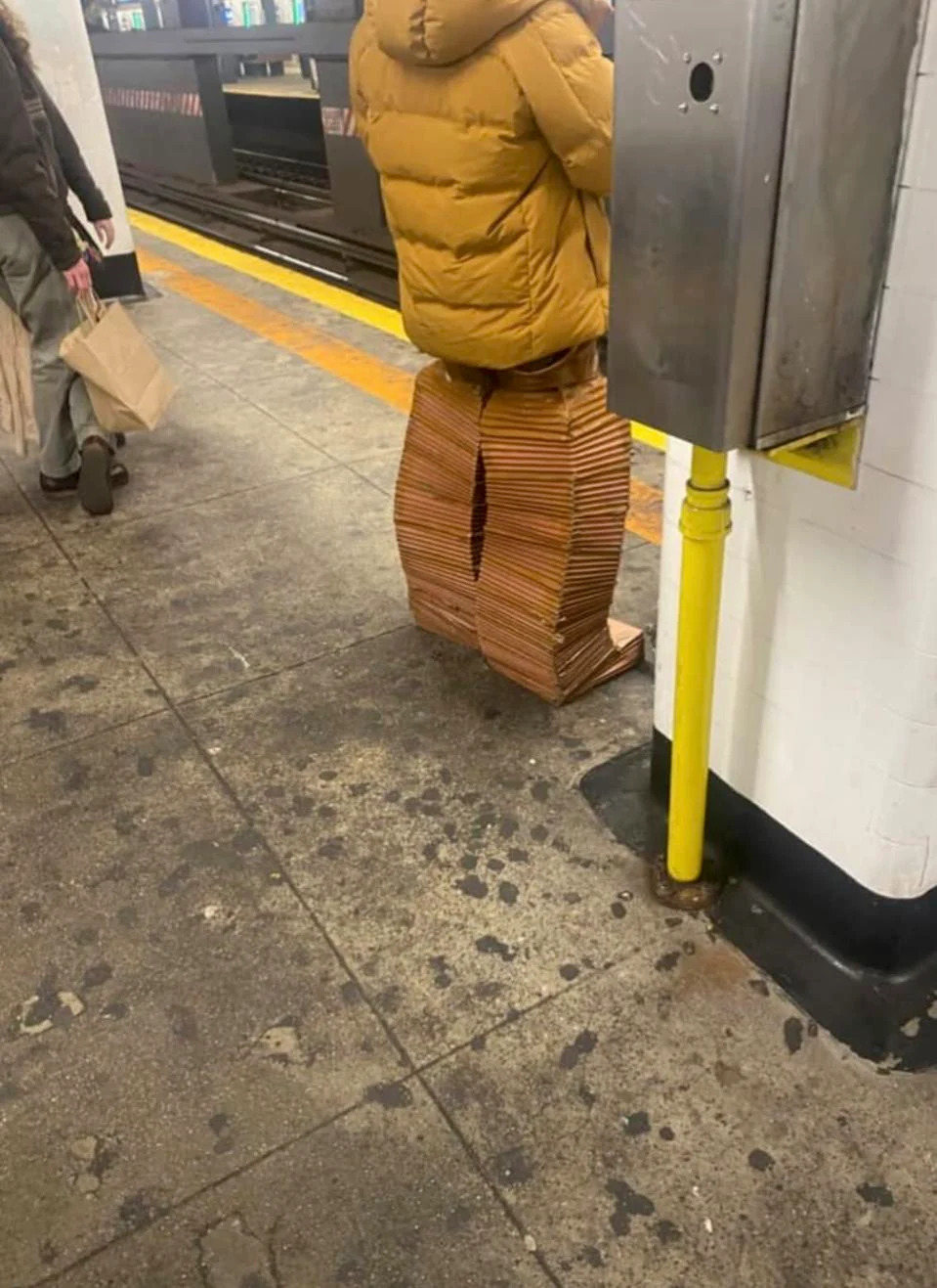 A man wearing odd pants is standing on a subway platform. 