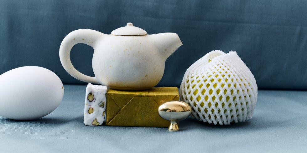 A collection of objects including a teapot, an egg, and a lemon wrapped in netting.