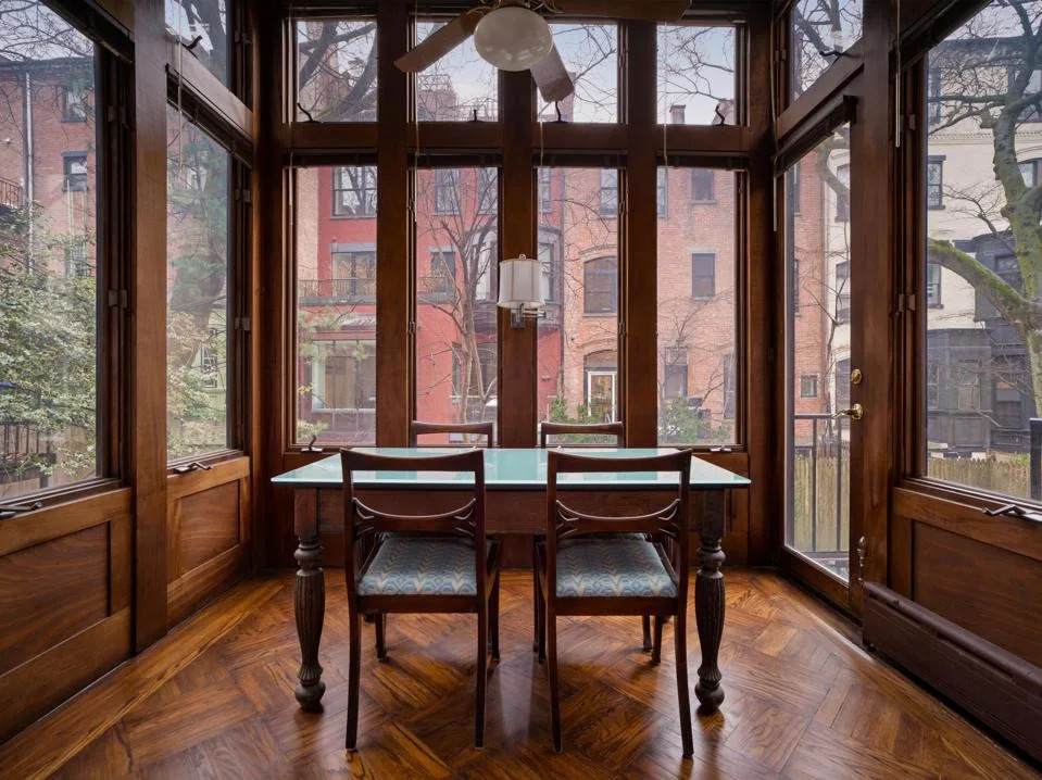 glass and wood sunroom with dining chairs overlooking back of row houses in Brooklyn