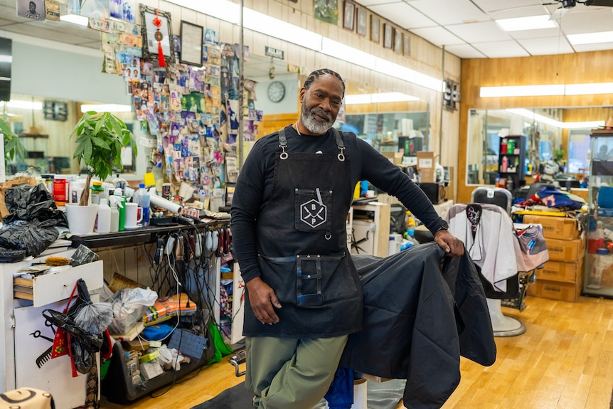 A man leans against a chair in a barber shop.
