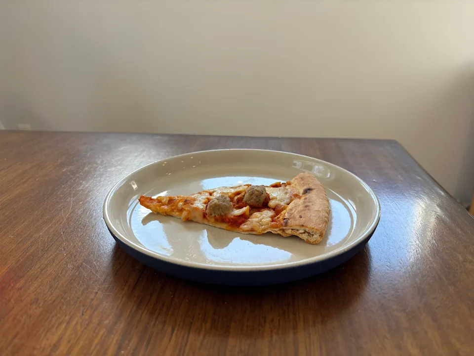 Slice of pizza with meatballs on a plate, placed on a wooden table