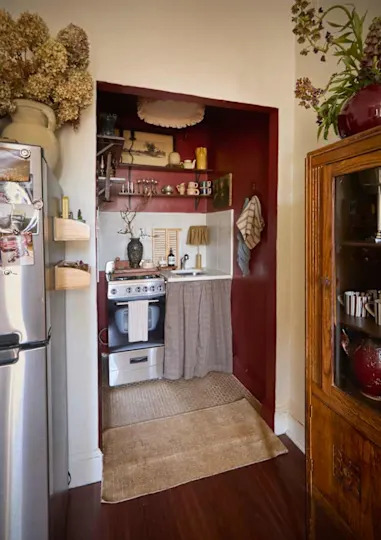 Cozy kitchen nook with a gas stove, sink, and wooden shelves displaying glassware and decor, accented by a red wall.