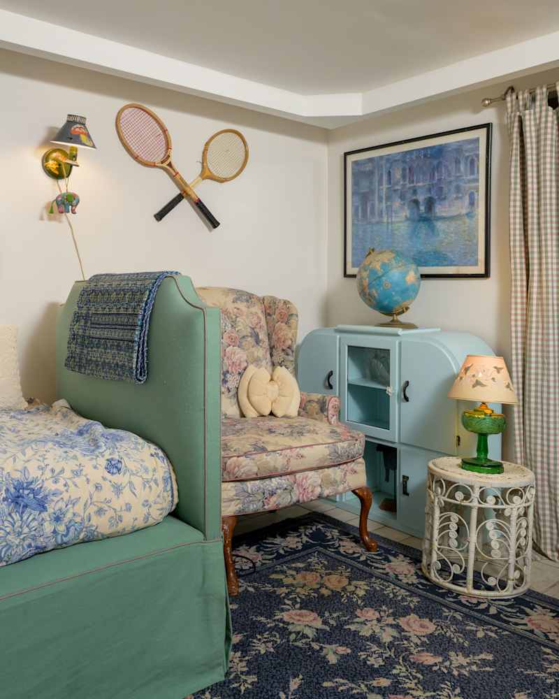 Cozy bedroom corner with a green bed, floral armchair, blue globe, and vintage tennis rackets on the wall.
