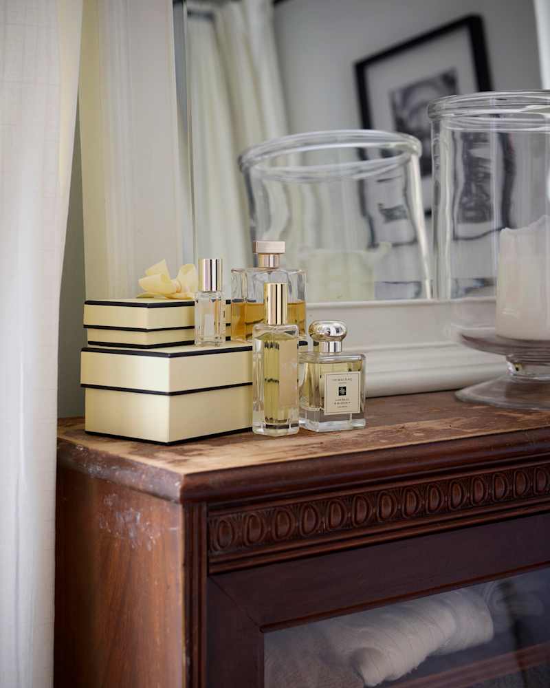 Perfume bottles on a wooden dresser with decorative boxes, a glass jar, and a candle.