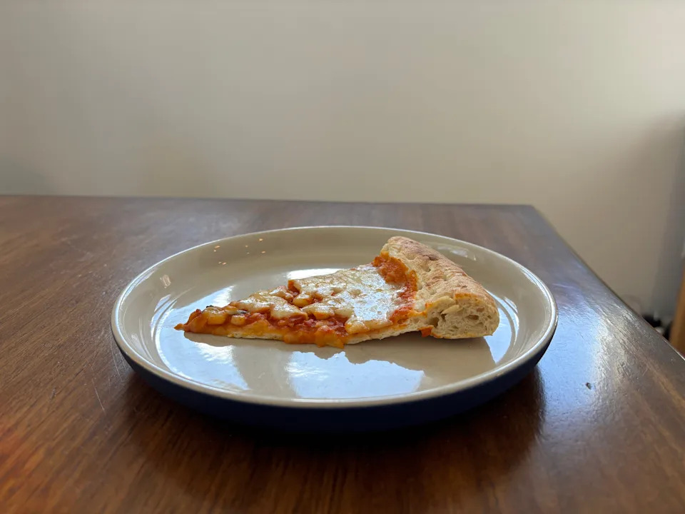 Slice of pizza with tomato sauce and cheese on a plate, resting on a wooden table