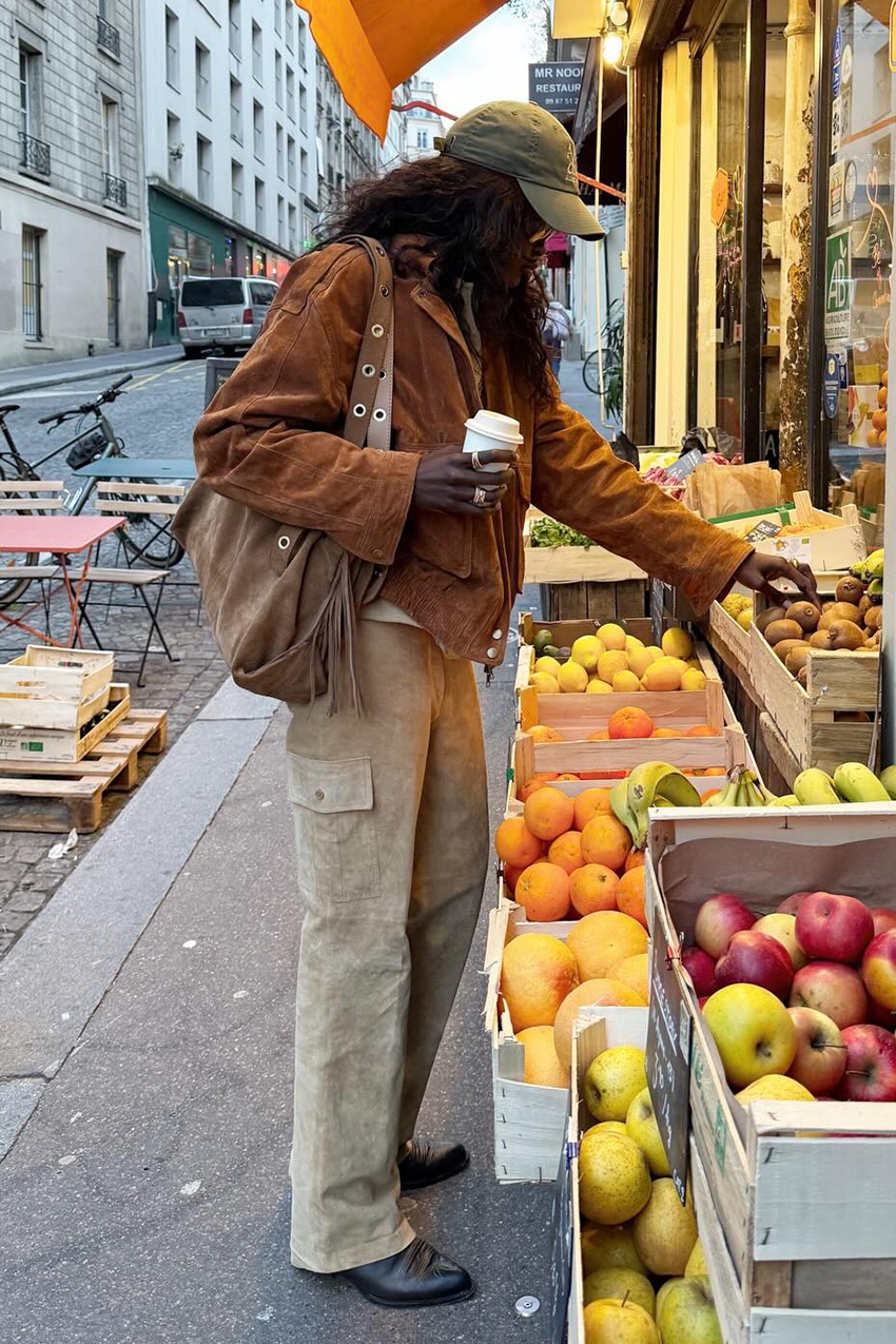 a woman wearing a suede tan jacket, beige cargo pants, black boots, and a brown suede fringe bag