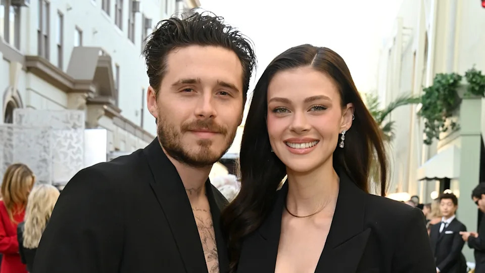 A man and woman smiling, dressed in black, standing outdoors.