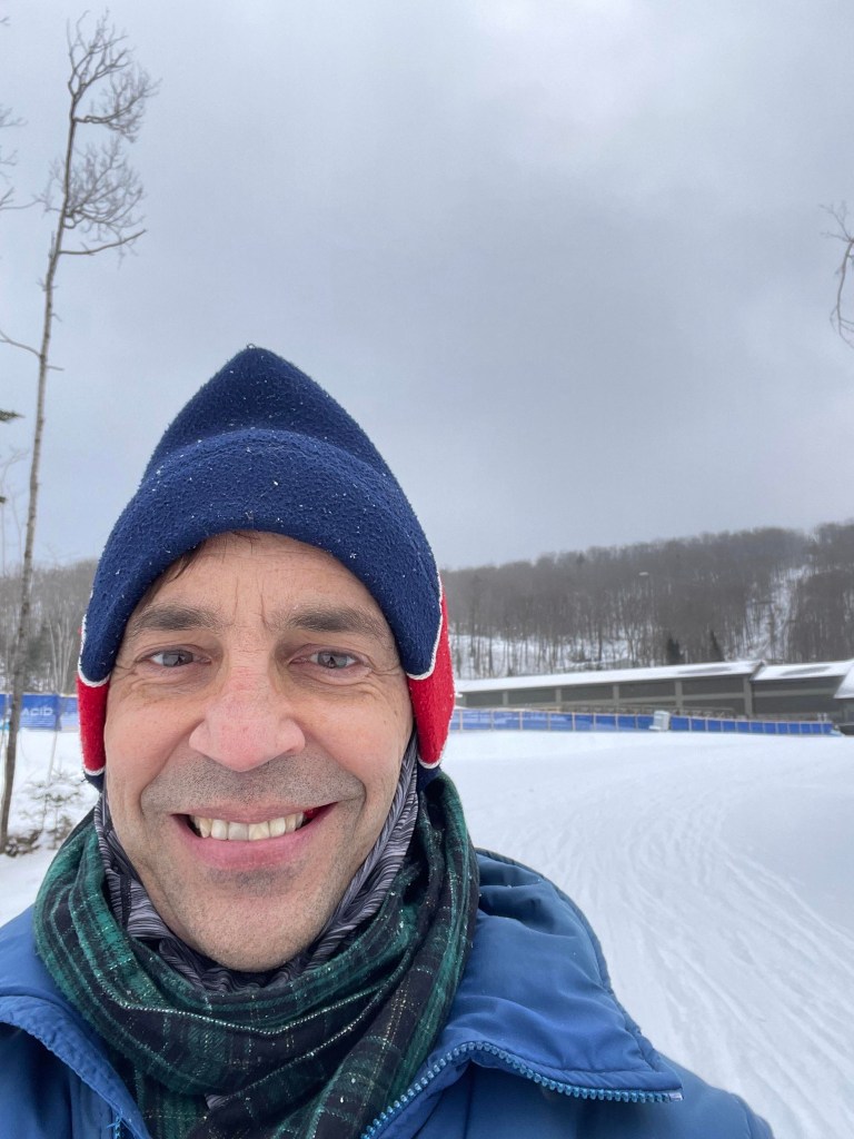 Douglas T. Von Hoppe in a blue hat and green scarf standing in a snowy landscape.