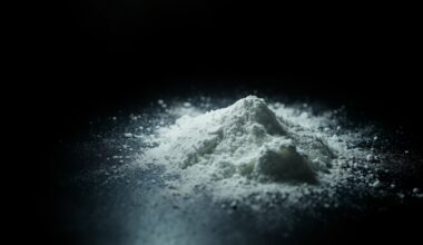 An extreme close-up photograph of a white, powdery substance on a dark surface, lit by a harsh, direct camera flash, creating a stark, gritty, and investigative aesthetic without depicting any violence or victims.