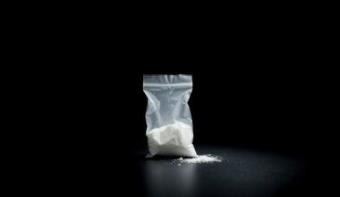 An extreme close-up of a small plastic bag containing a white powdery substance, dramatically lit by a harsh camera flash against a dark background, conceptually representing the drug charges that are keeping this defendant jailed despite the overturning of his murder conviction.