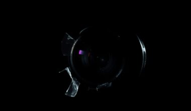 An extreme close-up photograph of a broken camera lens or other crime-related physical evidence, lit by a harsh, direct camera flash against a pitch-black background, creating a stark, gritty, investigative aesthetic.