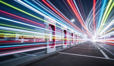 An abstract, blurred image of a Tesla Supercharger station, with streaks of vibrant colors representing the speed and motion of electric vehicle charging.