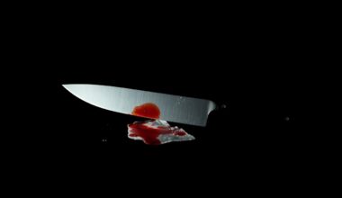 An extreme close-up photograph of a single piece of crime scene evidence, such as a knife or bloodied cloth, lit by a harsh, direct camera flash against a pitch-black background, conceptually representing the investigative work behind the arrest of a murder suspect.