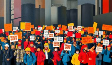 A dynamic, abstract painting of a crowd of protesters marching with union banners, the figures repeated in overlapping, geometric waves of bold primary colors against a dark, industrial background, capturing the energy and momentum of the labor movement.
