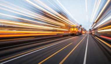An abstract, colorful image created with sweeping motion blur, depicting a construction vehicle or road crew working on M-50 in Brooklyn, conveying the dynamic energy and temporary disruption of the road improvement project.