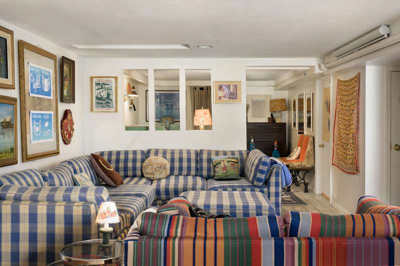 Cozy living room with blue and white checkered sofas, colorful striped cushions, and various framed artworks on the walls.