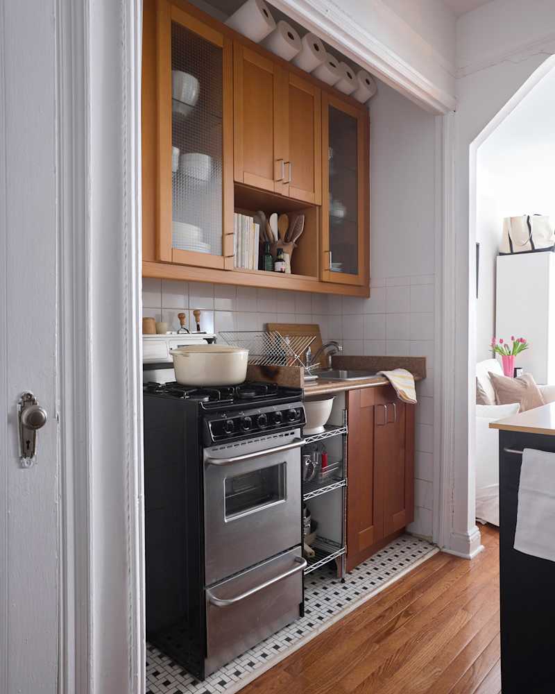 Compact kitchen with wooden cabinets, a black stove, sink, and a countertop, featuring a bowl and utensils.