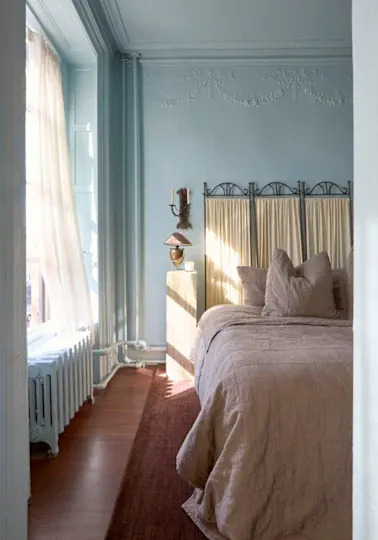 Cozy bedroom with a light blue wall, a bed with beige bedding, a wooden nightstand, and a vintage lamp.