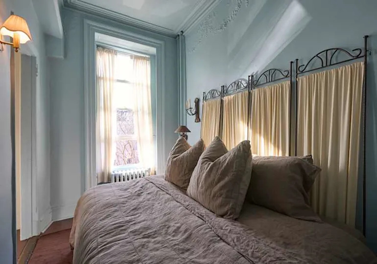 Cozy bedroom with a large bed featuring beige bedding and pillows, light curtains, and a window with a view.