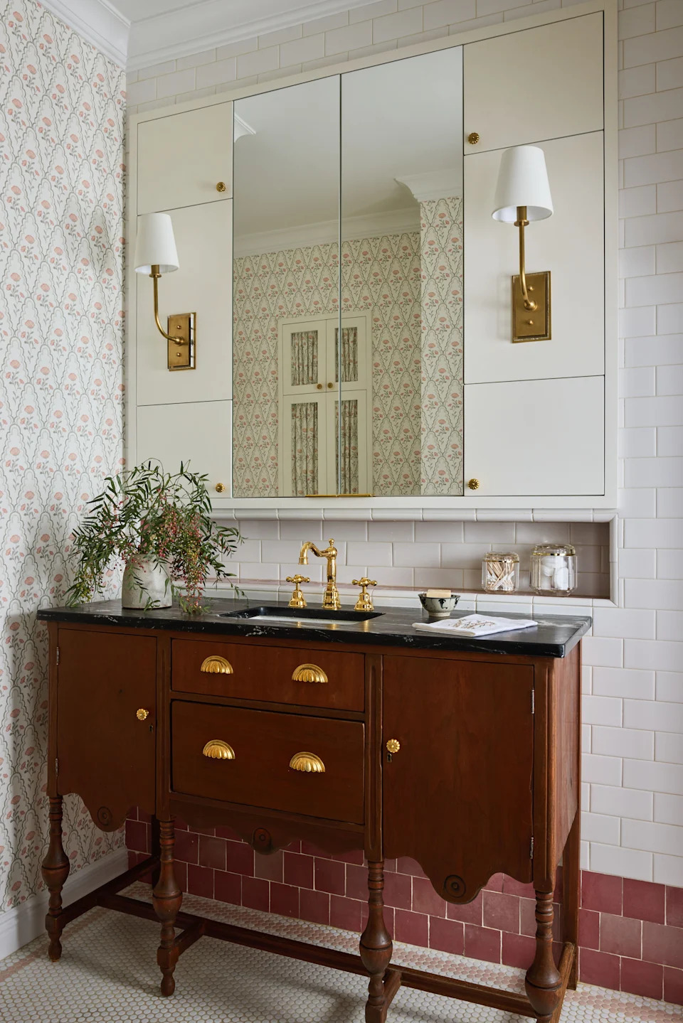 In the bathroom, a vintage vanity repurposed as a sink gives the room what Weed calls “a little dollhouse” quality. Pink-and-cream floral wallpaper from Stout Textiles carries through to Nemo Tile walls, Zia Tile trim, and a mosaic tile floor in a softly coordinated palette.