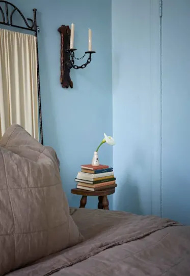 Cozy bedroom corner with a quilted bed, stacked books, and a small vase with a flower on a wooden side table.