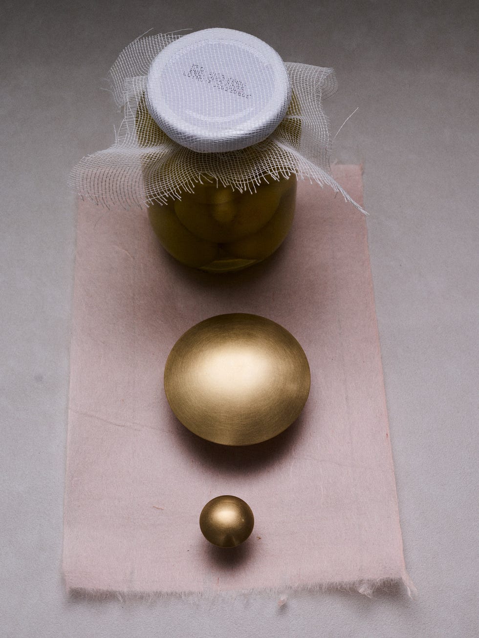 A jar of olives with two brass spheres on a soft fabric.