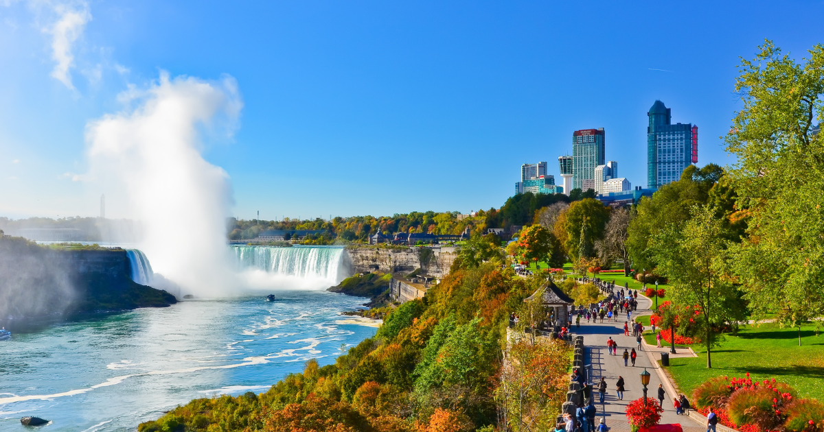 An aerial view of Niagara Falls, with people walking on a park path overlooking the falls.
