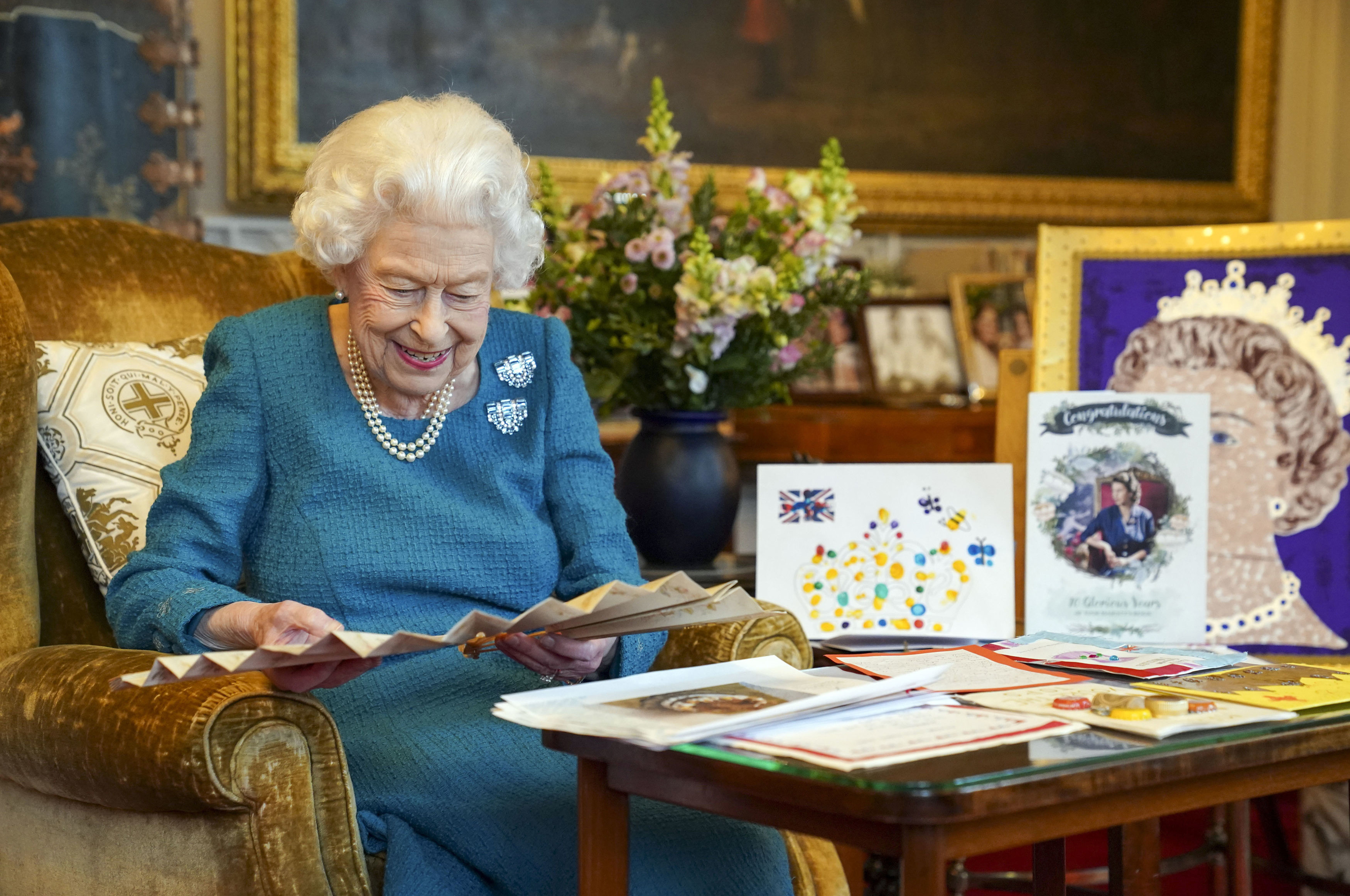 Queen Elizabeth wearing a teal dress looking at cards