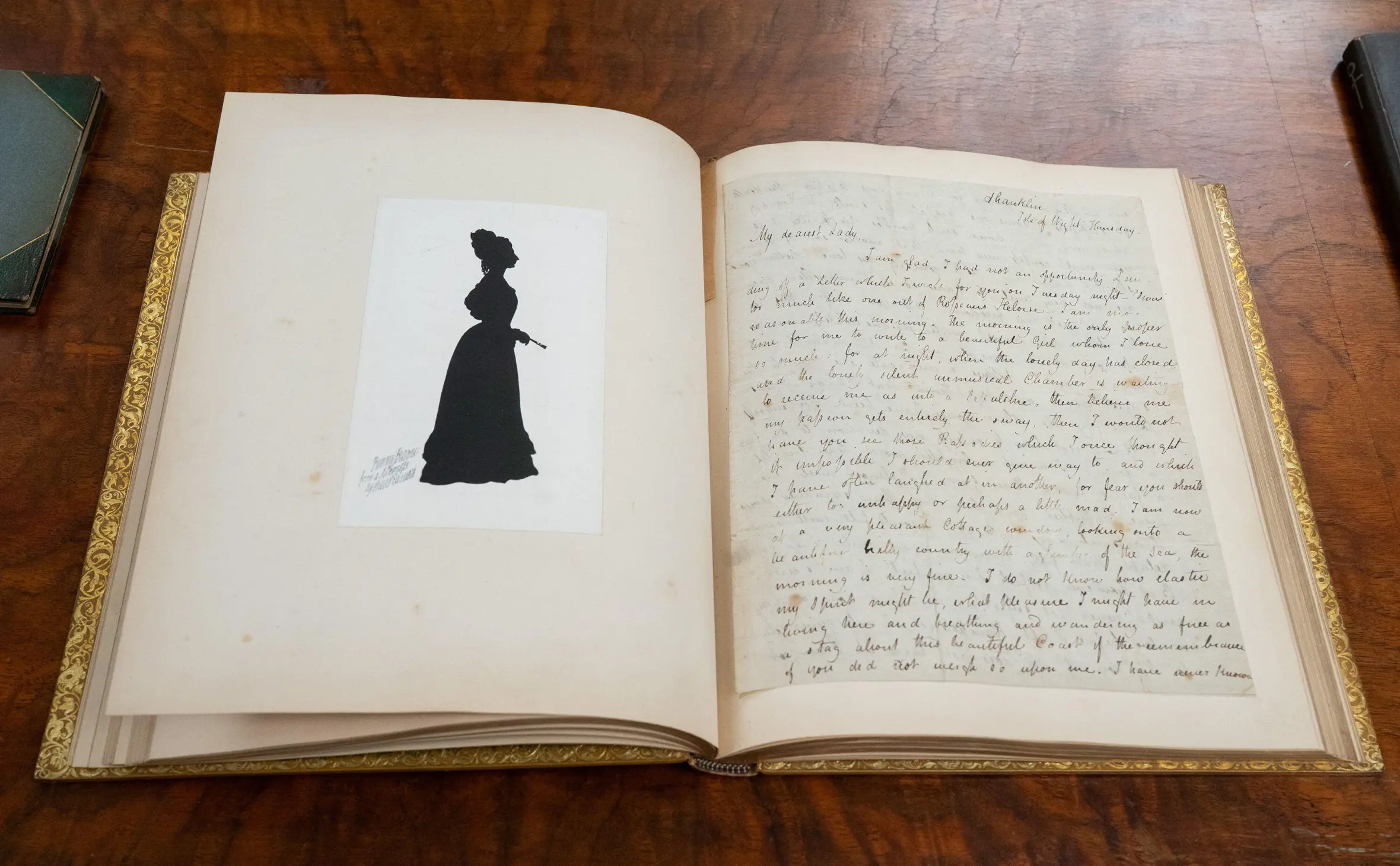 A bound collection of 37 love letters by John Keats to Fanny Brawne, opened to display a handwritten letter and a silhouette illustration of a woman in a dress.