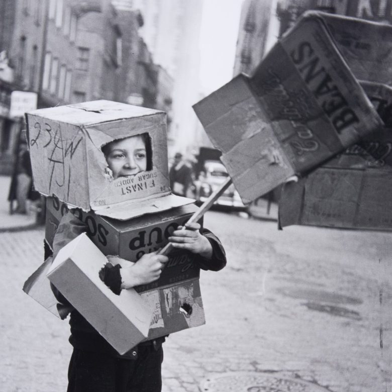 Black and white street photo of a boy wearing cardboard boxes as a costume, from the Bronx Boys photography exhibition at The Breman in Atlanta.